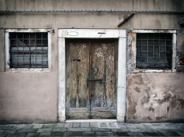 faded old run down empty house in venice with cracked walls and bolted peeling wooden door with bars on windows