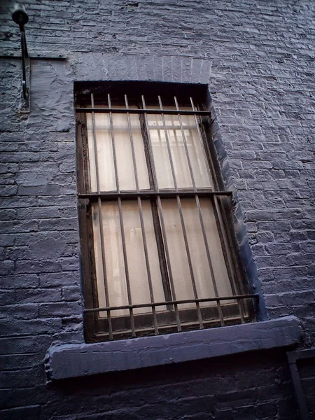 Slanted image of an old metal window with metal bars in a black painted wall — Stock Photo, Image
