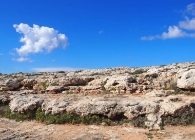 çatlaklar ve beyaz bulutlar ile mavi güneşli gökyüzü bitki örtüsü ile engebeli kayalık kurak kireçtaşı kaldırım manzara
