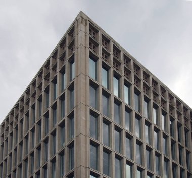 Gri bulutlu gökyüzüne karşı geometrik beton iskeleti olan 1960 'ların tipik vahşi tarzı bir beton ofis binasının köşesi.