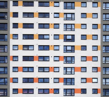 Yüksek katlı bir apartmanın pencerelerinin tam kare görüntüsü. Beyaz duvarlı, turuncu ve gri detaylı pencereler.