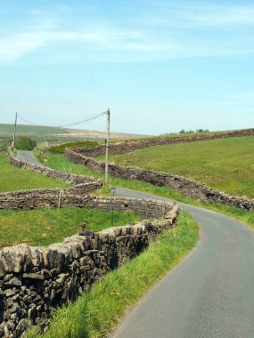 Yorkshire Dales kırsalının kuru taş duvarlarıyla çevrili dolambaçlı dar bir kırsalda kavşak. Eski Howarth yolunda mavi gökyüzü var.