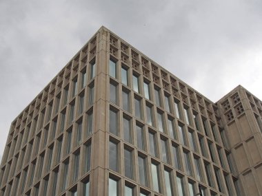 Gri bulutlu gökyüzüne karşı geometrik beton iskeleti olan 1960 'ların tipik vahşi tarzı bir beton ofis binasının köşesi.