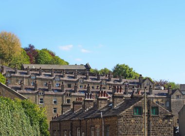 streets of terraced stone houses on a hillside surrounded by trees with a blue summer sky in hebden bridge west yorkshire clipart