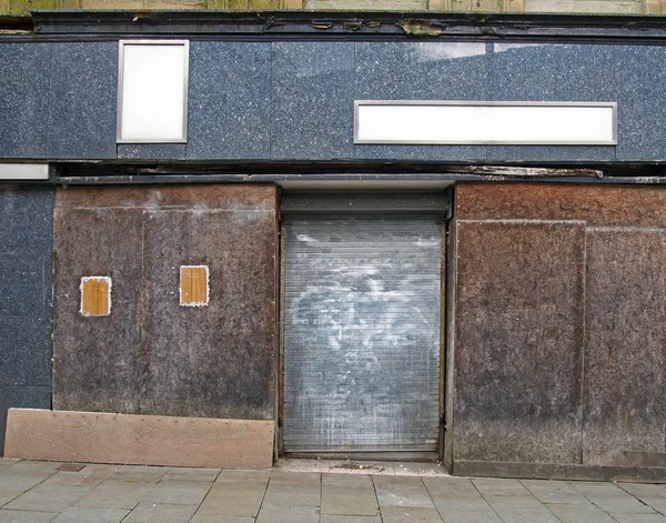 Ein Straßenblick auf die Front eines alten, verlassenen Ladens mit verfallenden, vergitterten Fenstern, die das Schaufenster bedecken, und einem geschlossenen Stahlverschluss — Stockfoto