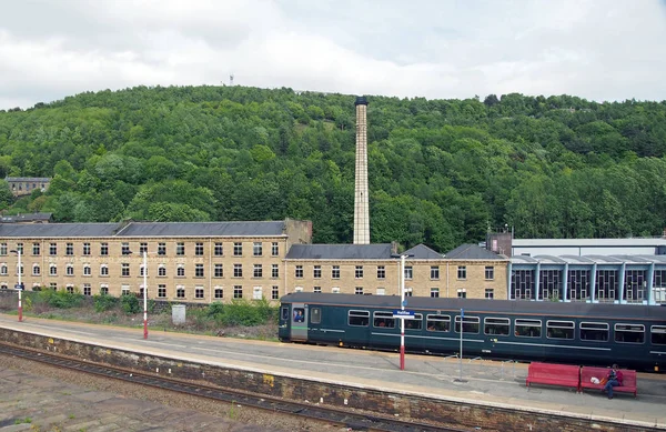 Ett tåg som kör in till järnvägsstationen halifax i västra Yorkshire med omgivande byggnader och trädbeklädda kullar, — Stockfoto