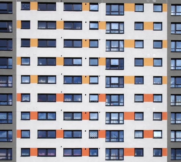 Yüksek katlı bir apartmanın pencerelerinin tam kare görüntüsü. Beyaz duvarlı, turuncu ve gri detaylı pencereler.