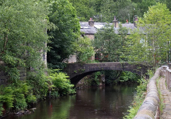 Una passerella che attraversa il fiume Calder a Eastwood vicino al ponte di Ebden con una fila di case in pietra tra gli alberi della foresta — Foto Stock