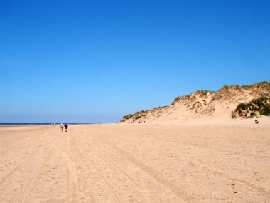 Sahilde yürüyen insanlar, deniz kenarındaki sefton sahillerindeki yüksek kum tepelerinin tepesinde çimenlerle mavi yaz denizi ve gökyüzüyle