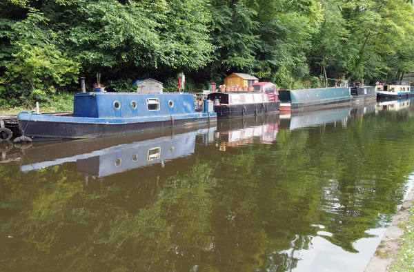 Schmale Boote und Lastkähne, die am Rochdale-Kanal in Hebden-Brücke festgemacht haben, umgeben von grünen Sommerbäumen — Stockfoto