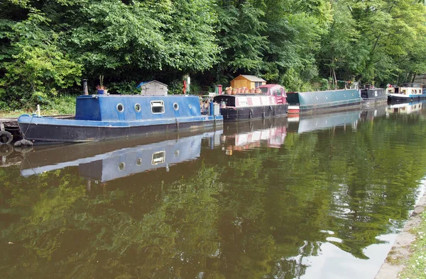 Úzké čluny a čluny kotvíné na kanálu Rochdalu v Hebden Bridge obklopené zelenými letní stromy — Stock fotografie