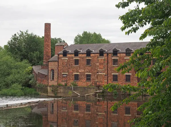 Die Thwaite-Mühle wurde 1825 auf einer Insel zwischen dem Fluss aire und dem ruhigeren Schifffahrtskanal erbaut, der sich im Wasser spiegelt und von Bäumen umgeben ist — Stockfoto