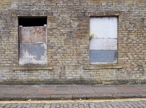 Frontansicht eines alten, verlassenen Hauses an einer leeren Straße mit vergitterten Fenstern und maroden Ziegelwänden — Stockfoto