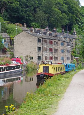 Hebden Köprüsü 'nden geçen Rochdale Kanalı' nın demirli tekneleri sulara ve ağaçlarla çevrili taş binalara yansıyor.