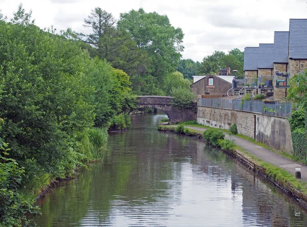 Une passerelle en pierre traversant le canal rochdale dans mytholmroyd avec des maisons au bord de l'eau entourées d'arbres — Photo