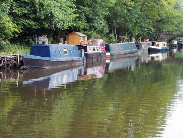 狭窄的小船和驳船停泊在河床桥上的罗奇代尔运河上，周围环绕着绿色的夏季树木和一座石桥 — 图库照片