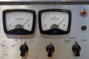 Kontrol düğmeleri ve düğmeleri olan eski bir makaranın iki desibel ölçer görüntüsü.