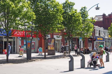Chapel caddesi Merseyside 'daki dükkanlarda yaya geçidinde yürüyen insanlar ve bebek arabasında bebekle yeşil saçlı genç bir anne.