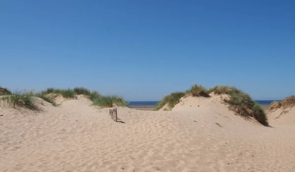 Песчаные дюны с небольшим деревянным забором против голубого летнего неба в форме на берегу Мерсисайда — стоковое фото