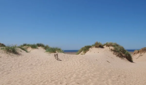 Dunas de arena cubiertas de hierba con una pequeña valla de madera contra un cielo azul de verano en Formby en la costa de Merseyside — Foto de Stock