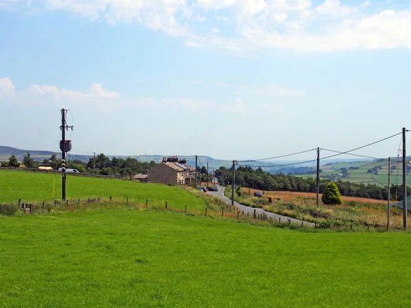 Casas na aldeia de Blackshaw cabeça no oeste de yorkshire com uma estrada correndo campos de pensamento com fazendas distantes e colinas pennine contra um céu azul de verão — Fotografia de Stock