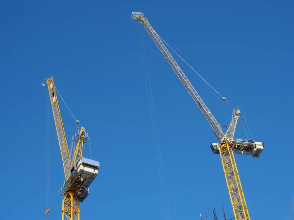 Mavi gökyüzüne karşı inşaat alanında çalışan iki uzun sarı vinç. — Stok fotoğraf