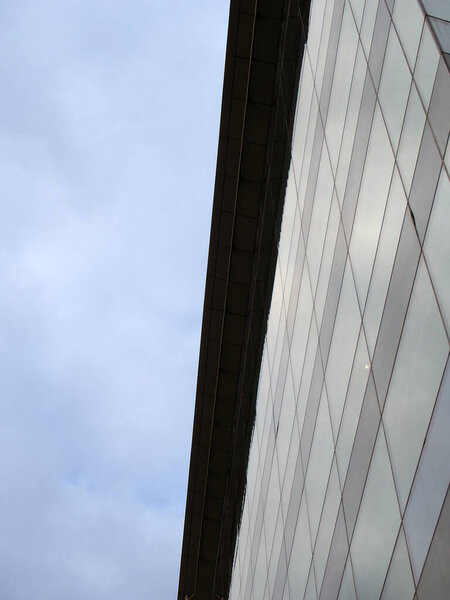 Vertical upwards view of a modem office building with a blue cloudy sky on one side reflected in the windows