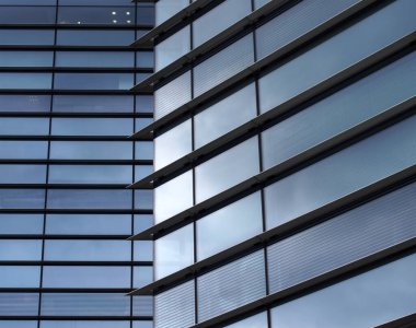 Geniş camlı pencerelerde mavi gökyüzünü yansıtan yüksek binaların geometrik şekilleriyle tam kare modern ofis mimarisi.