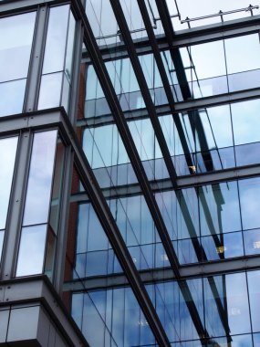 Geometrik şekilleri, binaları ve gökyüzünü mavi cam pencerelere yansıtan tam çerçeveli modern ofis mimarisi.