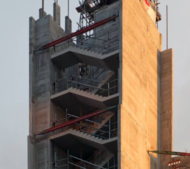 Mavi güneşli gökyüzüne karşı beton iskeleti olan yüksek bir inşaat sahasının tepesindeki bir vincin dikey görüntüsü