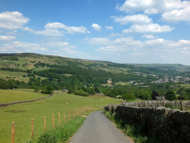 Batı Yorkshire Calder Vadisi 'ndeki orman ve tarlalarla çevrili Mytholmroyd kasabasını gören koyunlarla çevrili bir kır yolu yokuş aşağı iniyor.