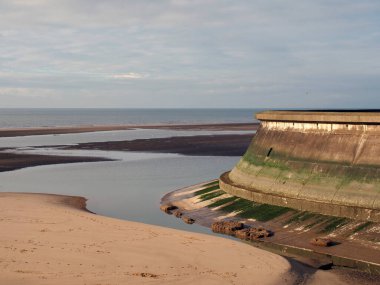 the concrete seawall of the old boating pool at blackpool lancashire surrounded by pools of water on the beach at low tide with a blue sea and clouds clipart