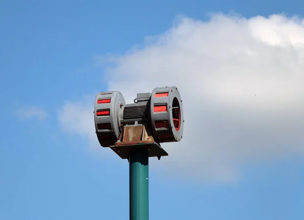 old mechanical warning siren on a pole against a blue cloudy sky