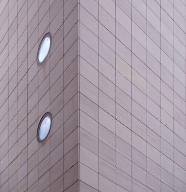 Gri dikdörtgen kaplamalı ve yuvarlak pencereli büyük, modern bir ticari binanın köşesi.