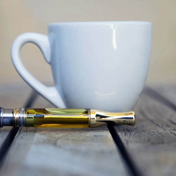 Vape Pen and cup on wooden surface, vaping marijuana oil, cannabis vaporizer
