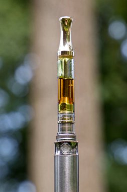 Marijuana oil for vaping on blurred natural background. clipart