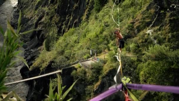 Extreem mannelijke balanceren op de Slack-lijn of Tightrope hoog boven de grond met groen bos en stromende rivier op de achtergrond — Stockvideo