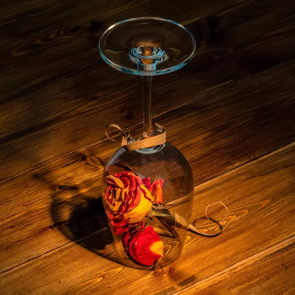 Inverted glass, in the interior of a dried rose, on the background of an old wooden table.