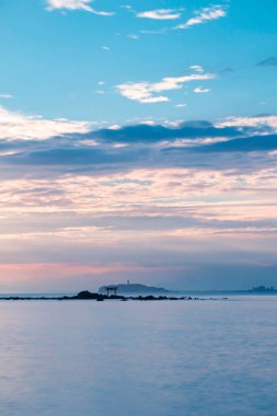 Denizin üzerinde ışık huzmesi. Uzakta Torii kapısı ve deniz feneri var. Portre yönelimi.