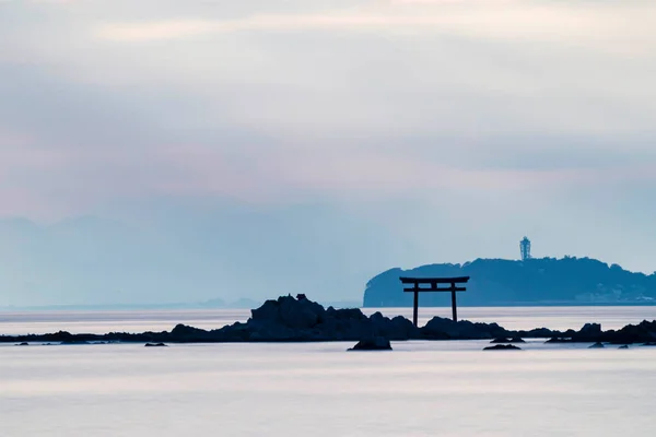 Denizin üzerinde ışık huzmesi. Uzaktaki Torii kapısı ve deniz feneri manzaralı.