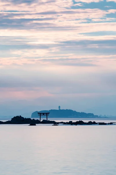 Denizin üzerinde ışık huzmesi. Uzakta Torii kapısı ve deniz feneri var. Portre yönelimi.