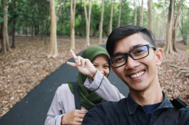 Asyalı bir erkek ve kadının, arka planda kamera tutarak fotoğraf çekerken çekilmiş bir portresi. Tatildeyken romantik ve mutlu bir ilişkide birliktelik