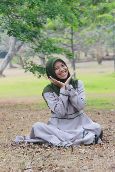 公園で遊んでいるアジア系女性の肖像画です ローブを着たイスラム教徒のモデルが幸せな表情で芝生の上に座っています — ストック写真