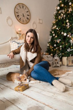 sıcak bir ceket kanepe önünde oturan ve Galce Corgi hırka, hediyeler dikkate alınarak bir köpekle oynayan bir kız