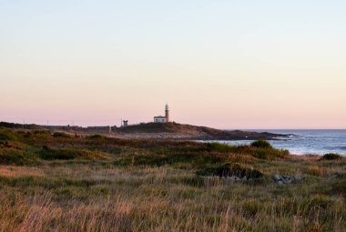 Deniz feneri günbatımı ışığı ile terk edilmiş. Galiçya, İspanya, güneşli bir gün, kırmızı ve mavi gökyüzü.