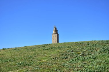 Herkül kule, komik bakış açısı. Çimenlerin üzerinde Roma deniz feneri. La Coruna, İspanya. Kamu parkı, güneşli bir gün, mavi gökyüzü.