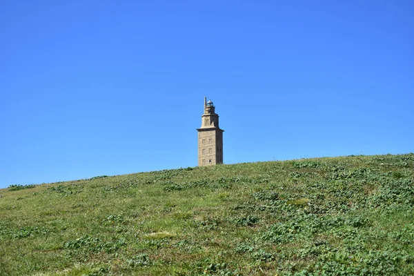 Herkül kule, komik bakış açısı. Çimenlerin üzerinde Roma deniz feneri. La Coruna, İspanya. Kamu parkı, güneşli bir gün, mavi gökyüzü.