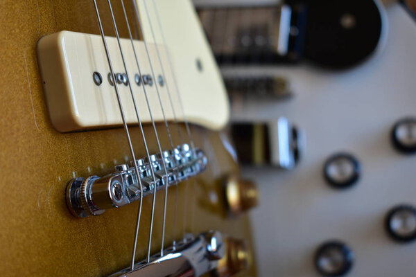 Gold top and white electric guitars closeup with P90 pickup. Body, pickups, bridge, strings, pickguard and knobs.