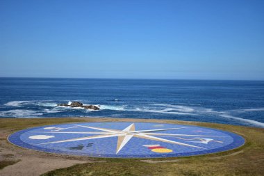 Rüzgar gülü ile deniz manzarası. Kayalar ve köpük mavi deniz. Güneşli bir gün, mavi gökyüzü, kamu parki. La Coruna, İspanya.