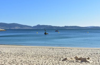 Plaj kum ve heykel kale ile. Parlak kum, açık su turkuaz renkli ve mavi gökyüzü ile. Güneşli bir gün. Sanxenxo, Galiçya, İspanya.